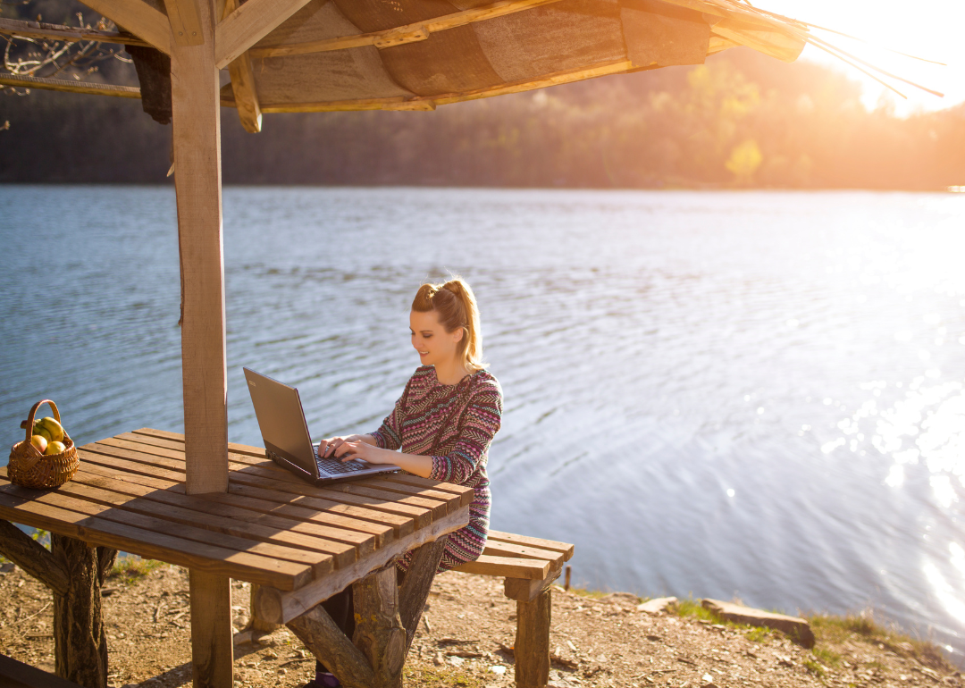 A person working on their laptop next to a picturesque lake