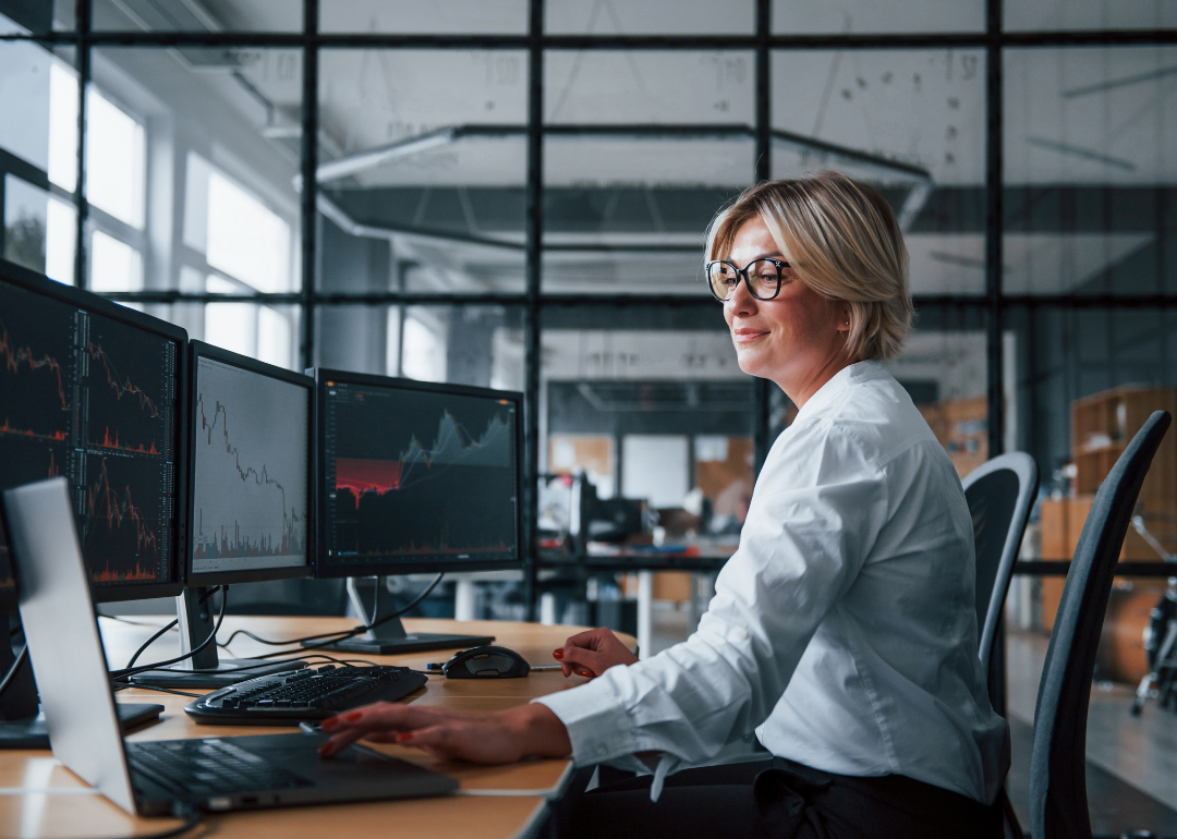 A white, female stockbroker sitting at a desk with multiple monitors.