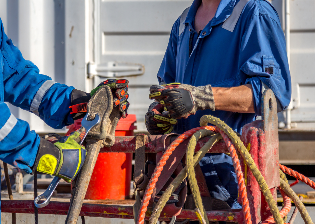 Oil rig workers using a wrench while working.