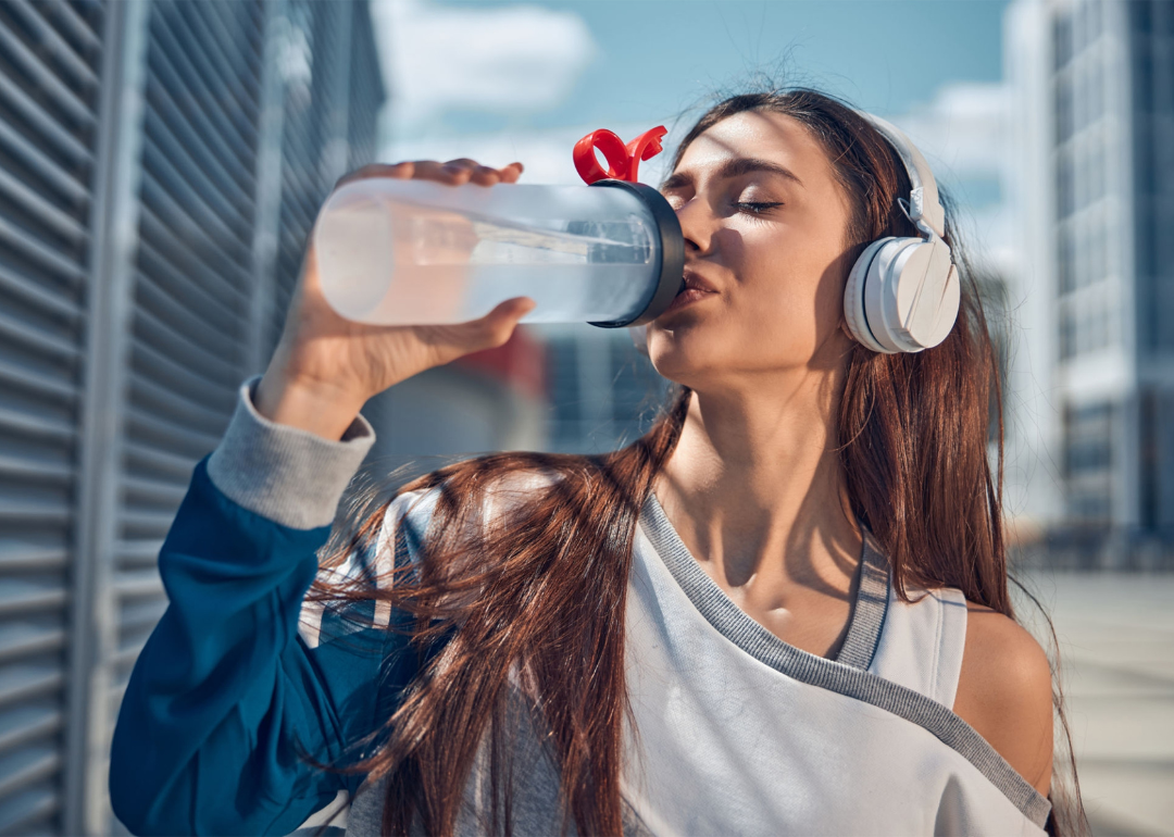 A person wearing headphones, drinking water, and walking.
