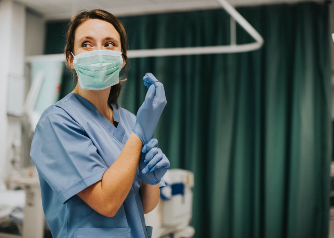 A woman nurse with a mask on putting on gloves.