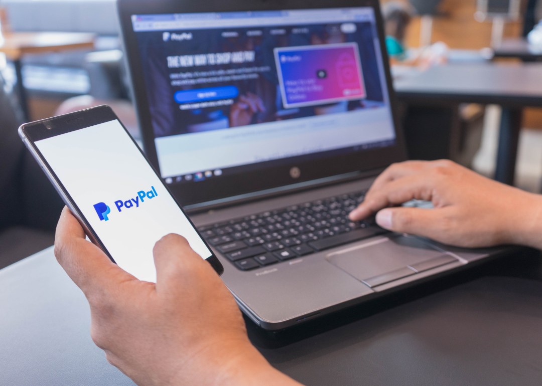 A person holding their phone open to PayPal in one hand while they browse the internet with the other.