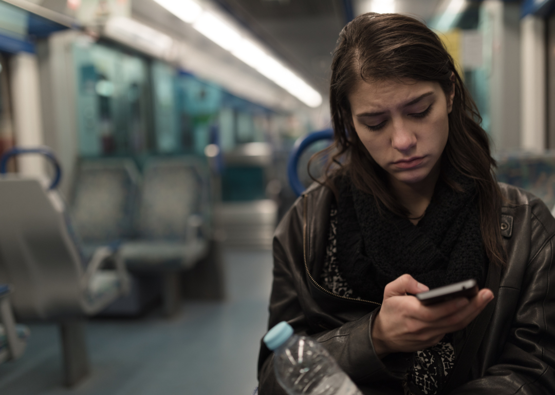 A young person using their phone while sitting alone and looking sad on the train