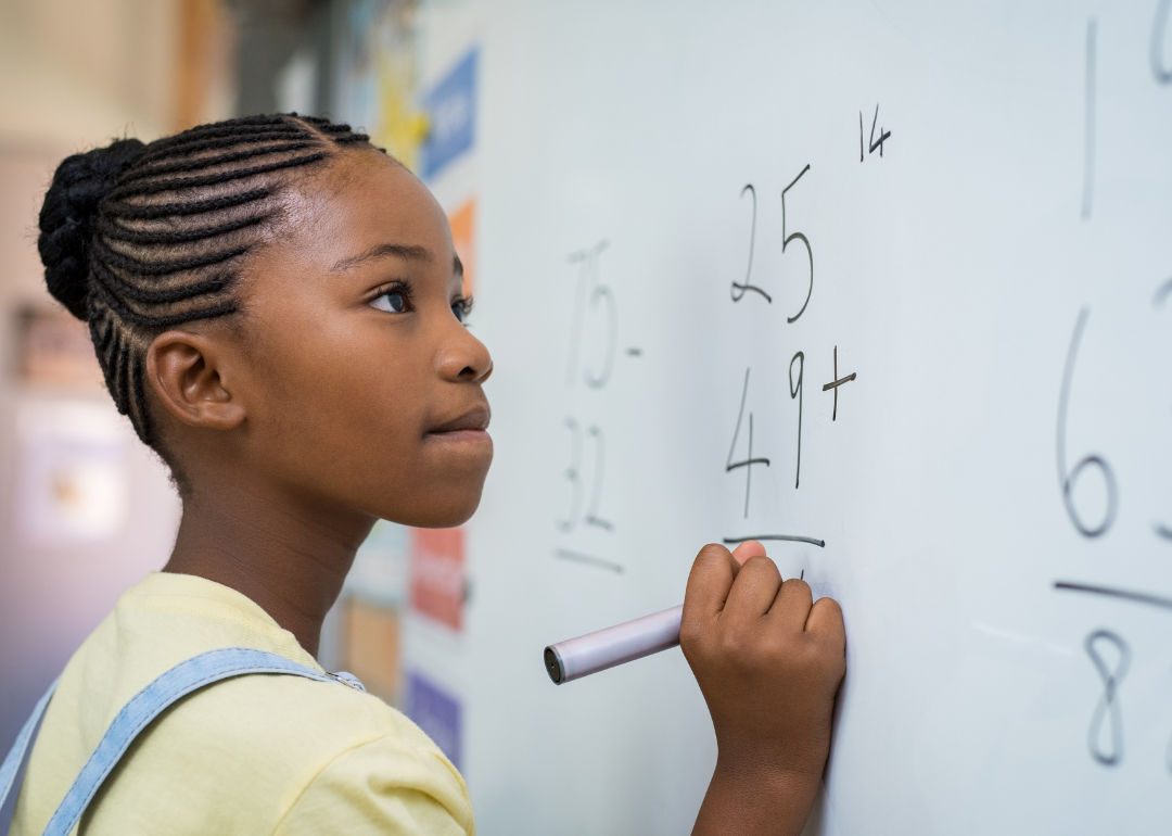 A student focusing while doing a math equation on a classroom's whiteboard.