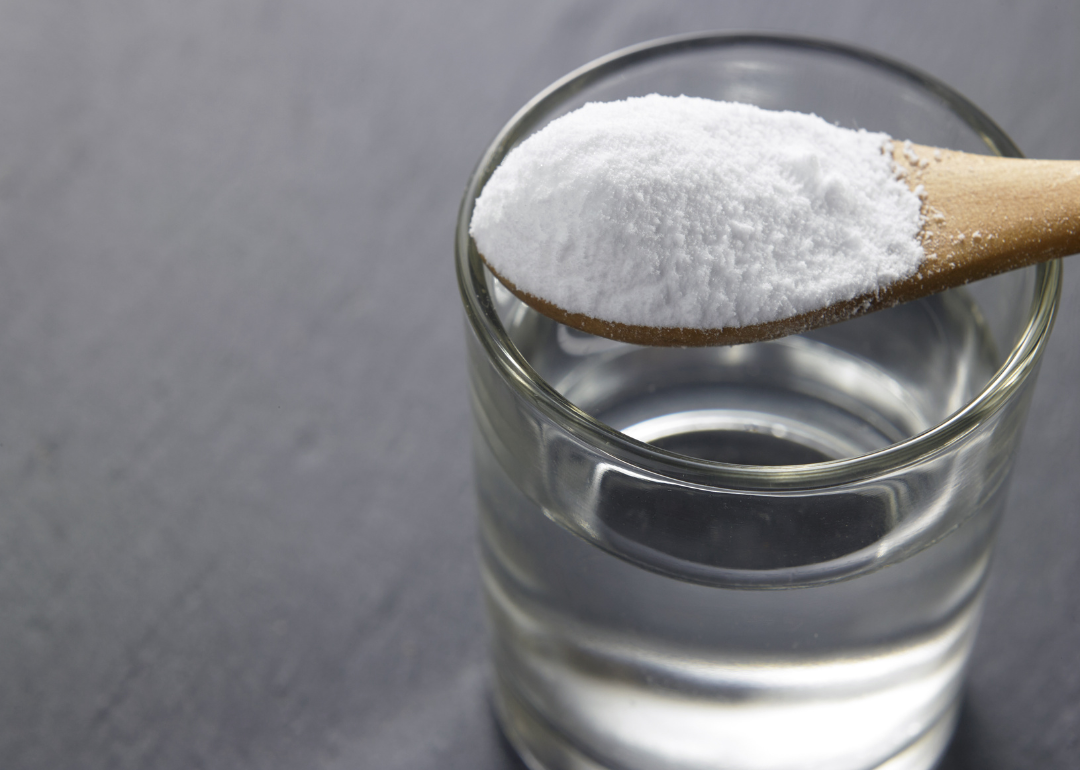 Baking soda being dropped in a glass of water to create a cleaning solution.