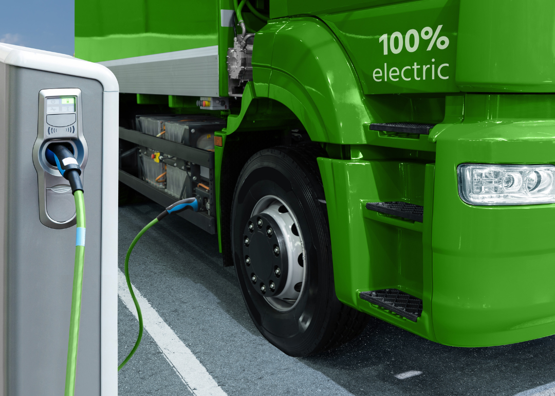 A green, electric truck charging in a parking lot.