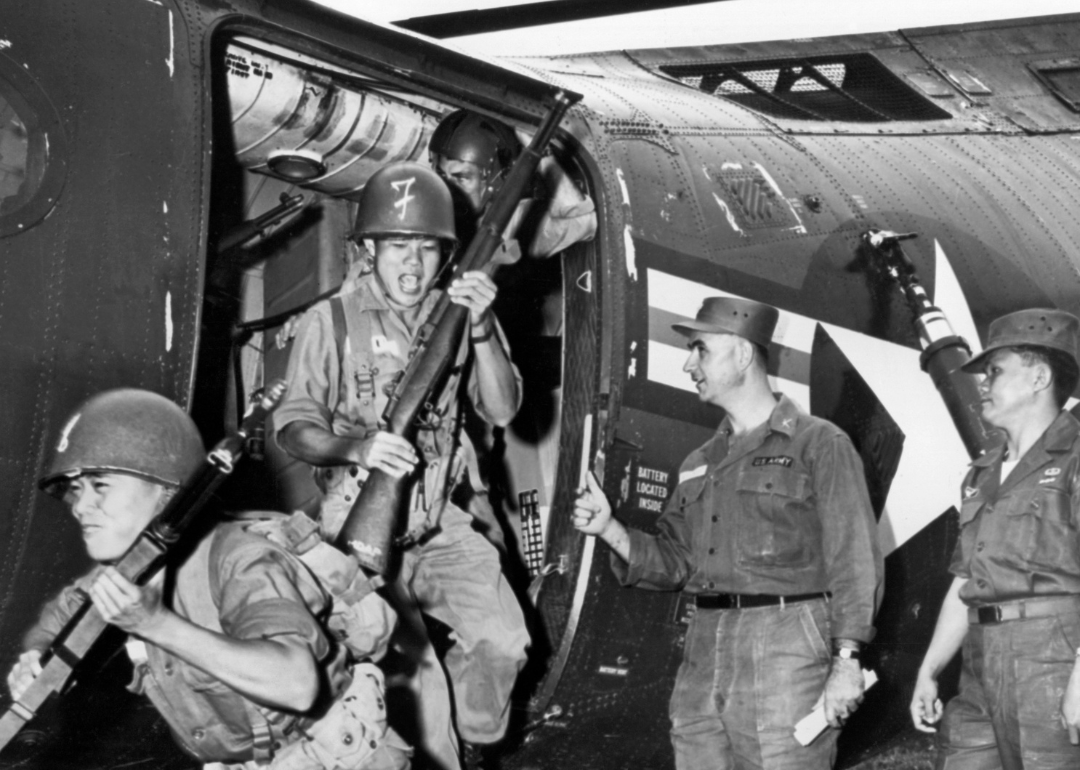 Vietnamese infantrymen pouring out of a Piasecki H-21C Shawnee helicopter as their US Army advisor instructors look on.