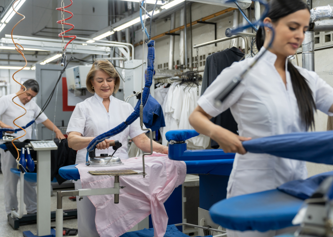 A group of workers at a laundry service ironing clothes
