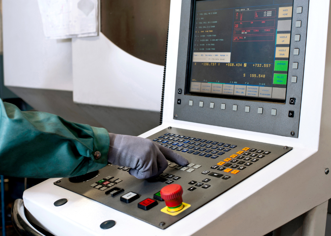 A technologist's hand on the control panel of a computer numerical control programmable machine in the milling industry.