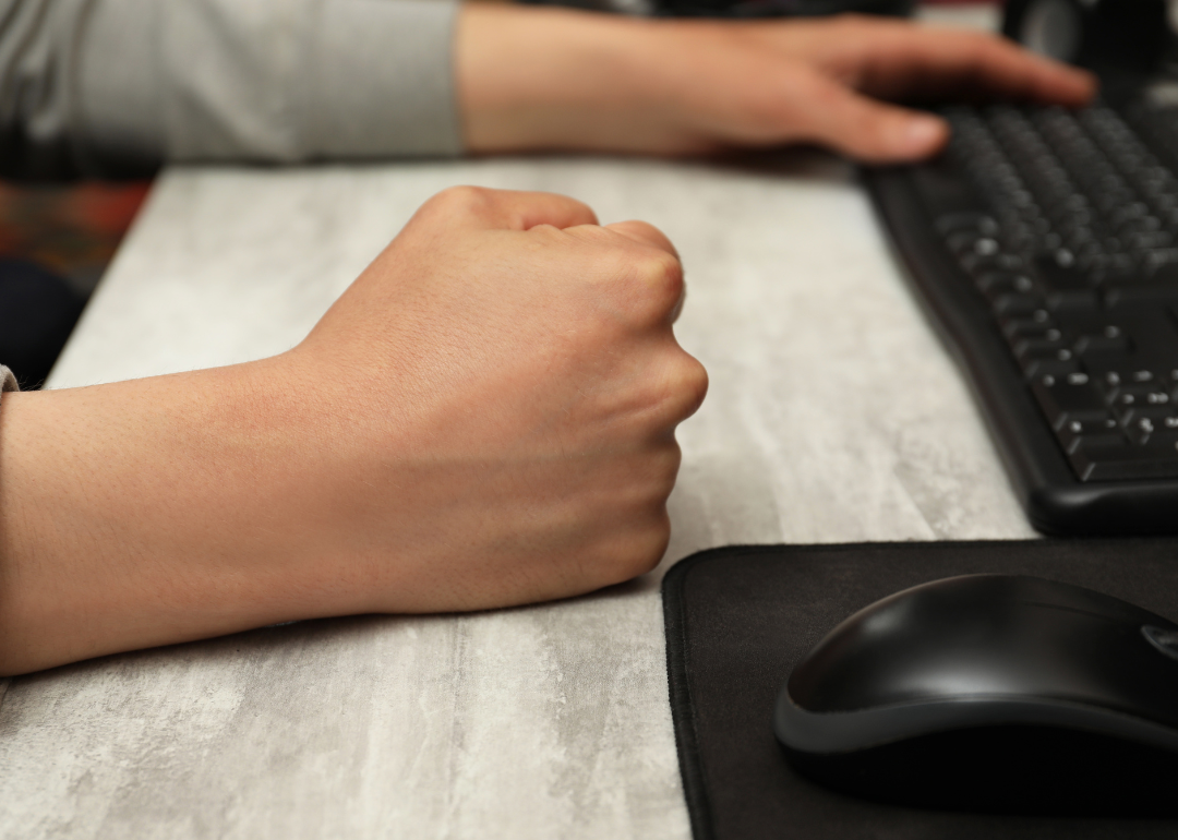 A close-up of a person with a clenched fist while on the computer.