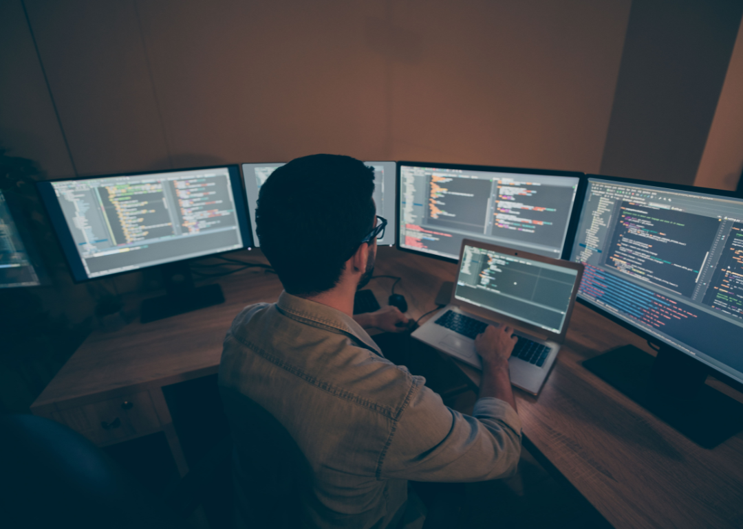 An employee sits at a desk that has four monitors.