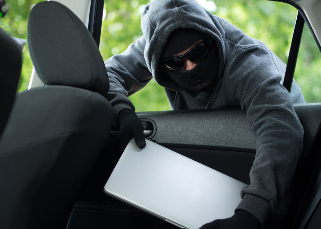 A person stealing a laptop through a car window.