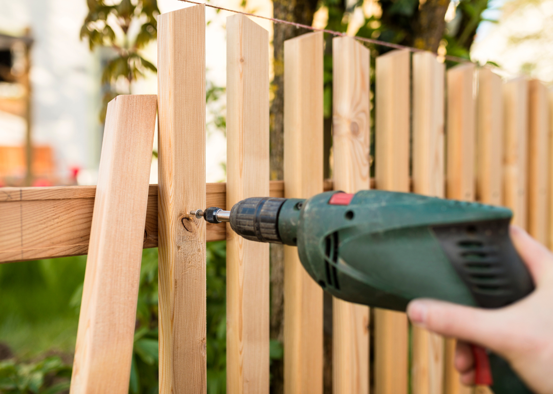 A person's hand using an electric drill to build a fence.
