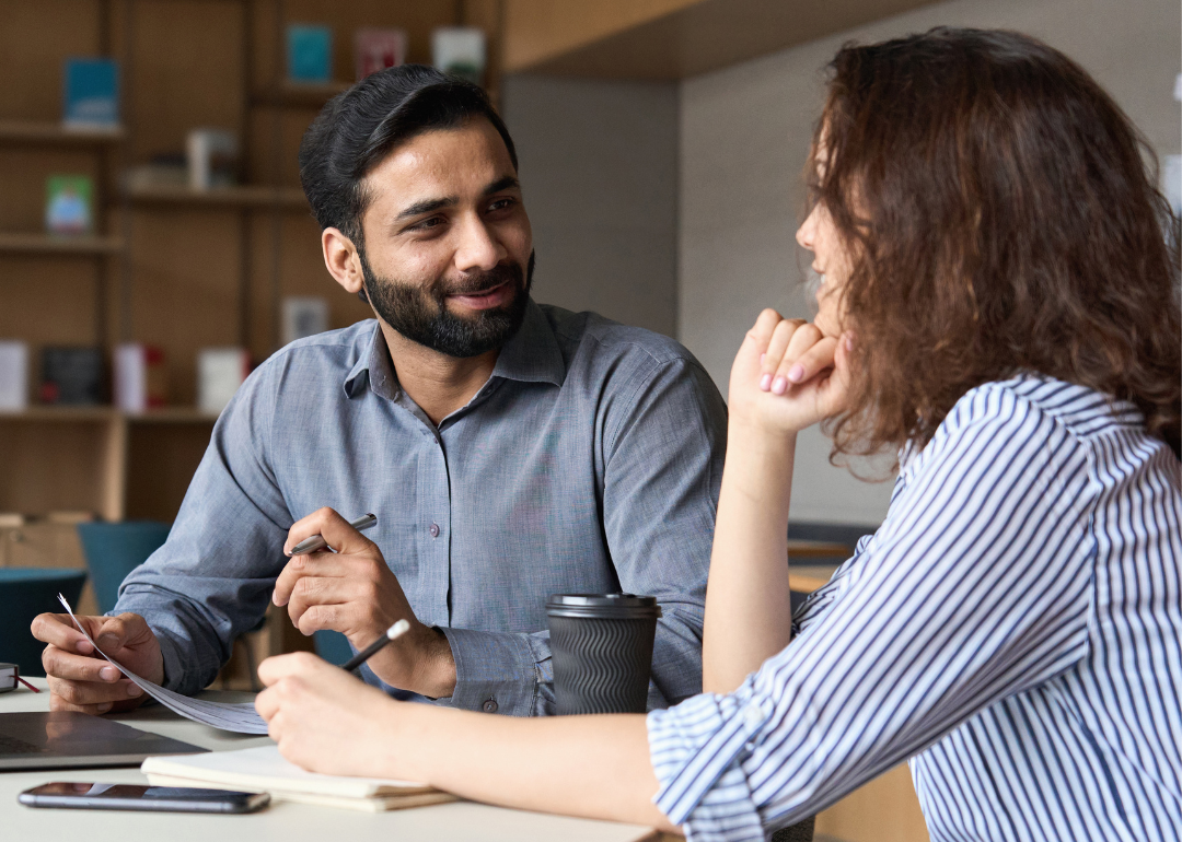 Two employees face each other at table while meeting one on one.