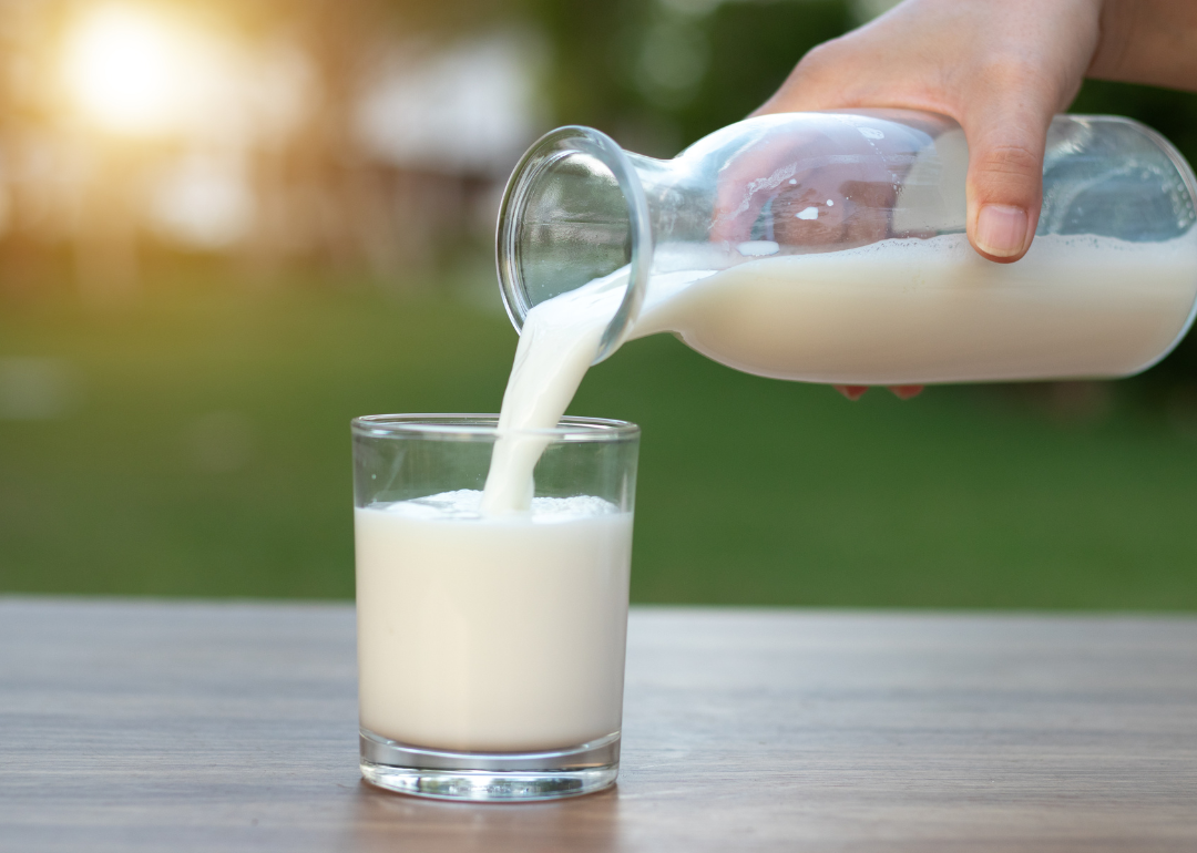 A hand pouring a bottle of milk into a glass.