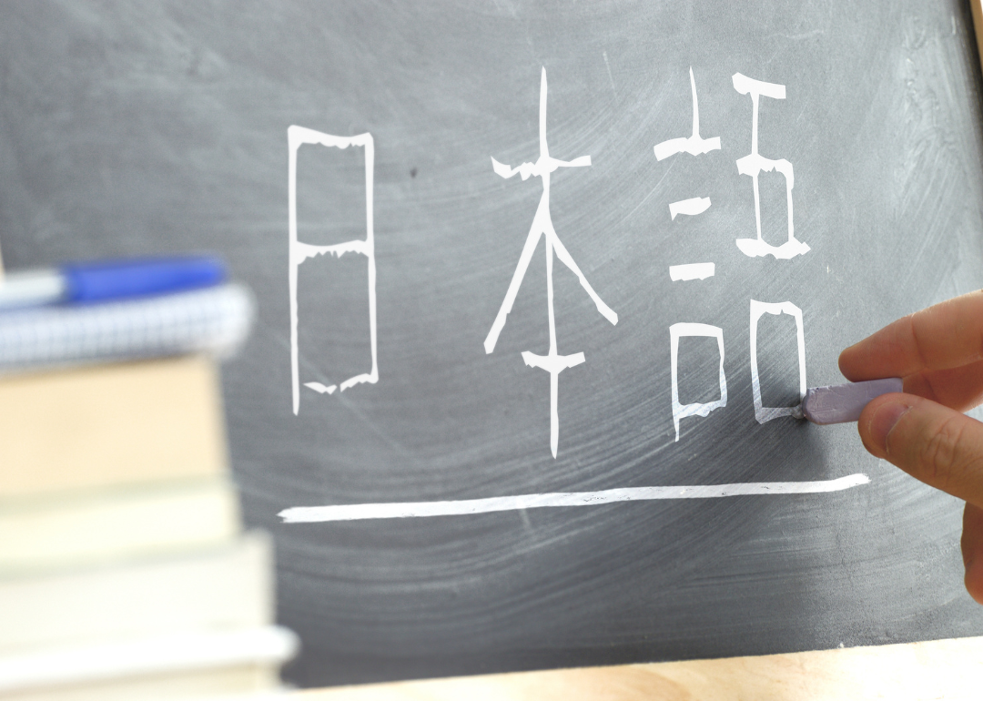 A hand writing the word "Japanese" in Kana syllabary on a blackboard in a Japanese class.