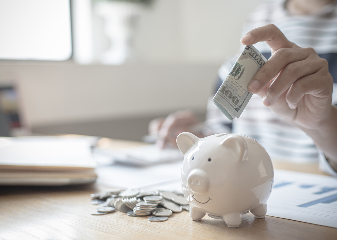 A person putting a $100 bill into a piggy bank.