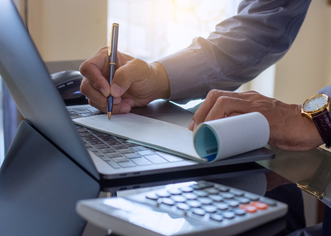 A business owner writing a check based on payroll data stored in their computer.