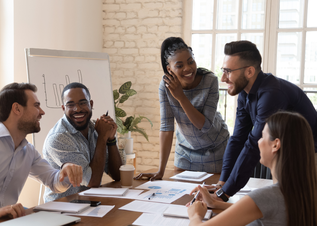 Smiling office workers sit together at a table in a meeting.