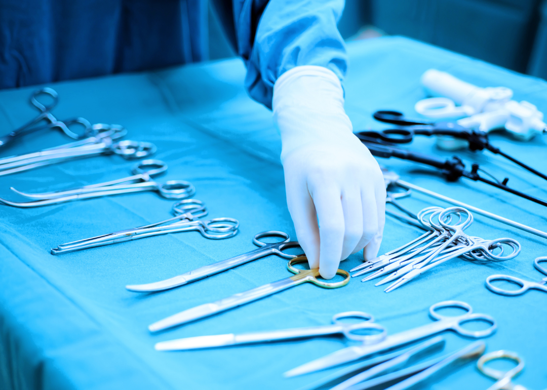 A doctor's gloved hand picking up a tool from a tray of surgical instruments.