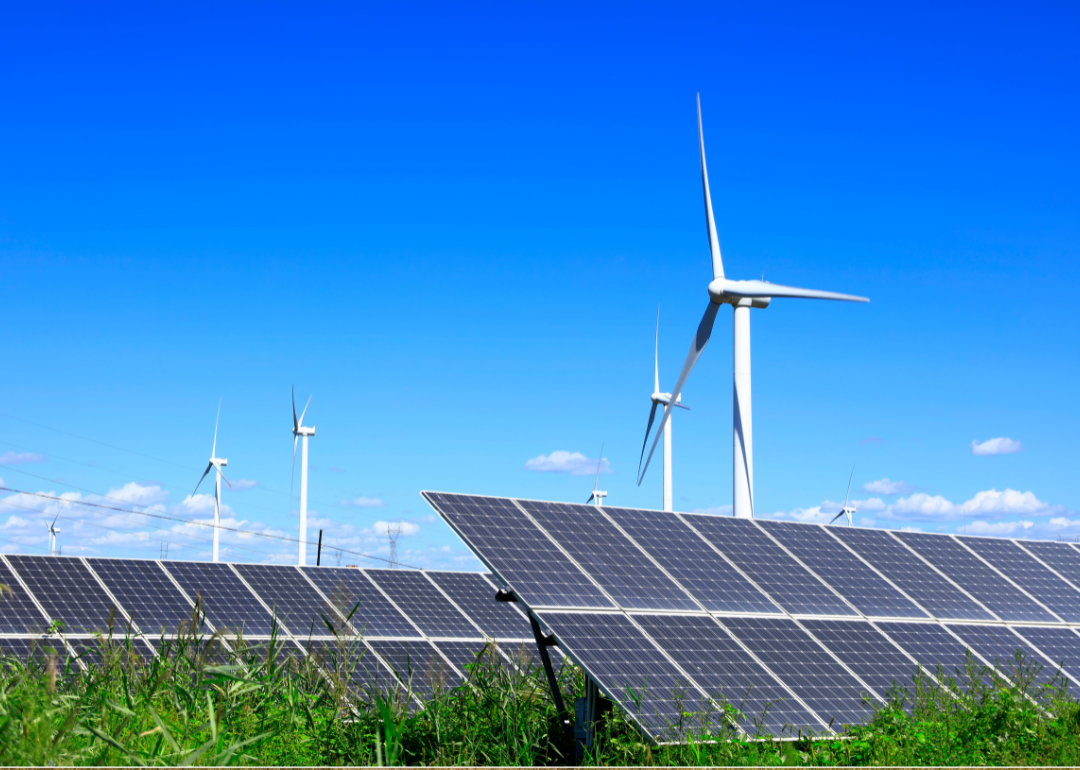 Solar photovoltaic panels and wind turbines under a clear, blue sky