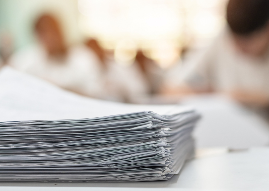 A stack of papers in front of a blurred classroom.
