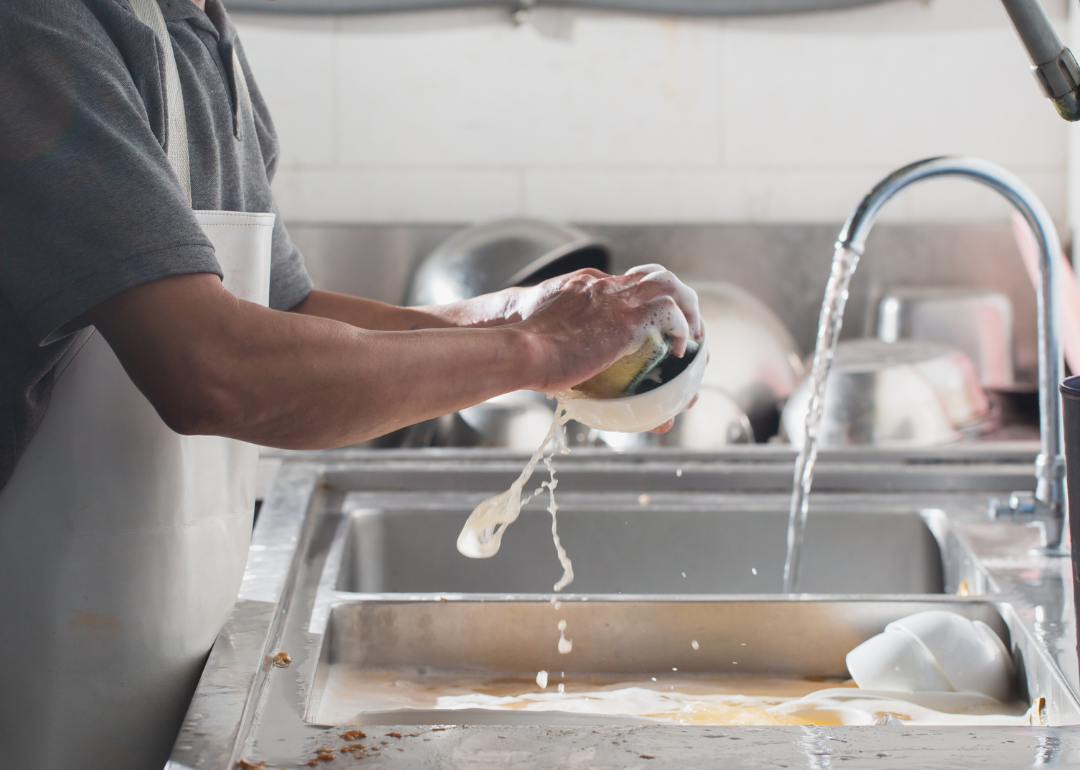 A worker cleans dishes over a sink.