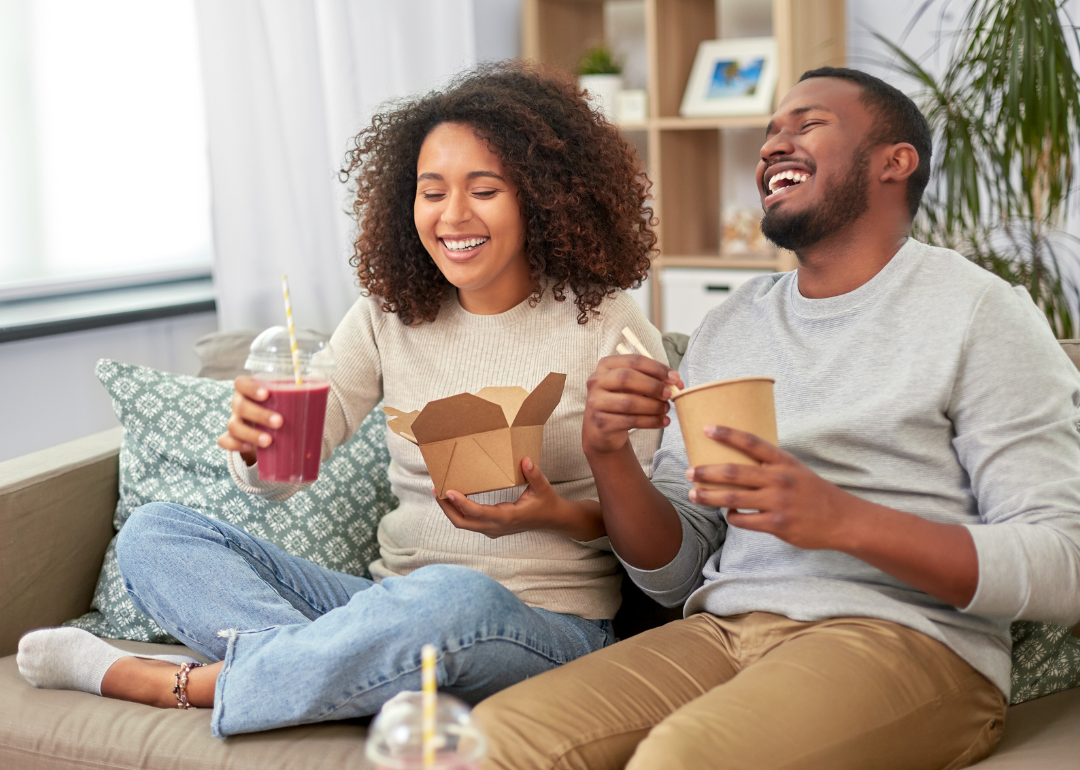 A happy couple eating takout food at home.