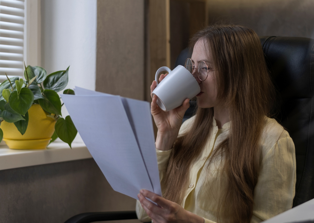 A teacher drinking coffee and reading a document.