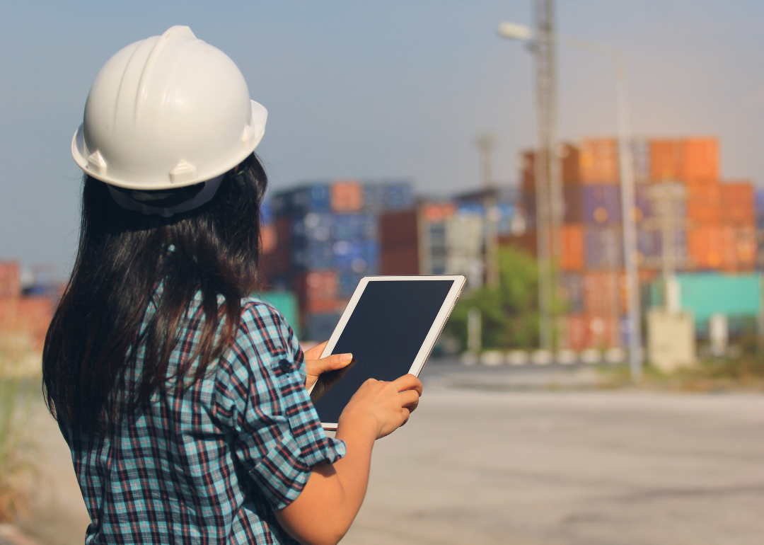 A supply chain logistician looking at shipment containers while holding an iPad.