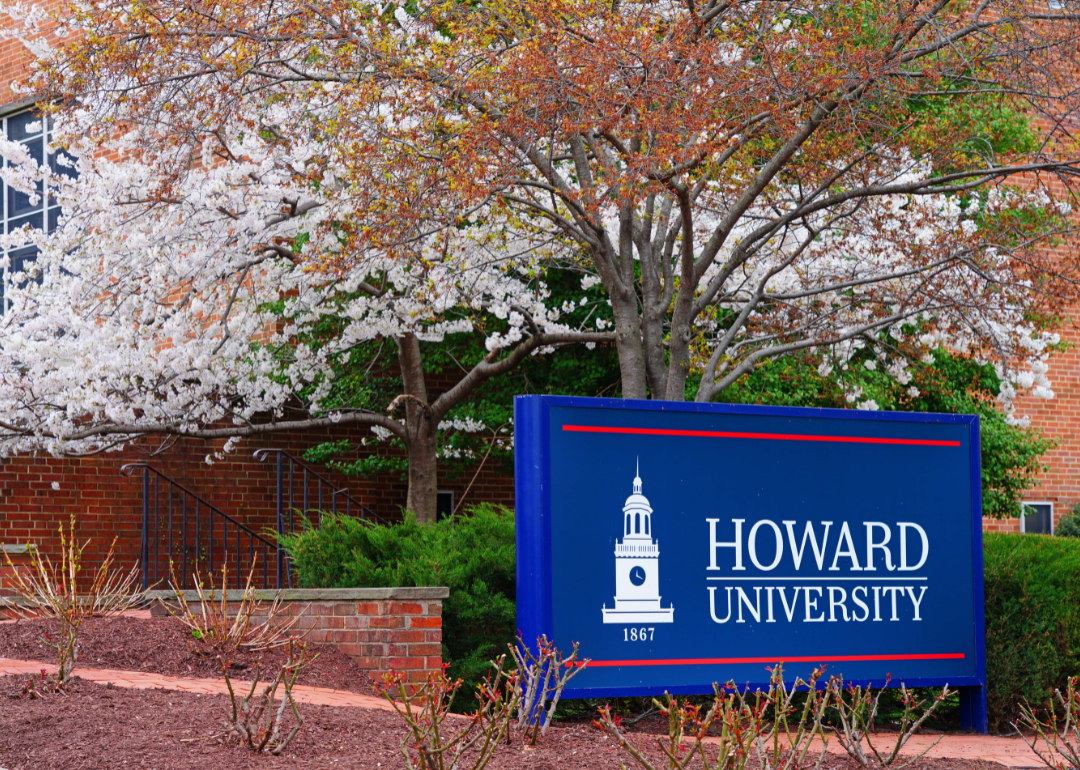 An entrance sign to Howard University with brick buildings in the background.