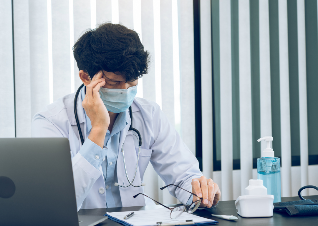 A doctor rubbing his head in stress while completing paperwork.