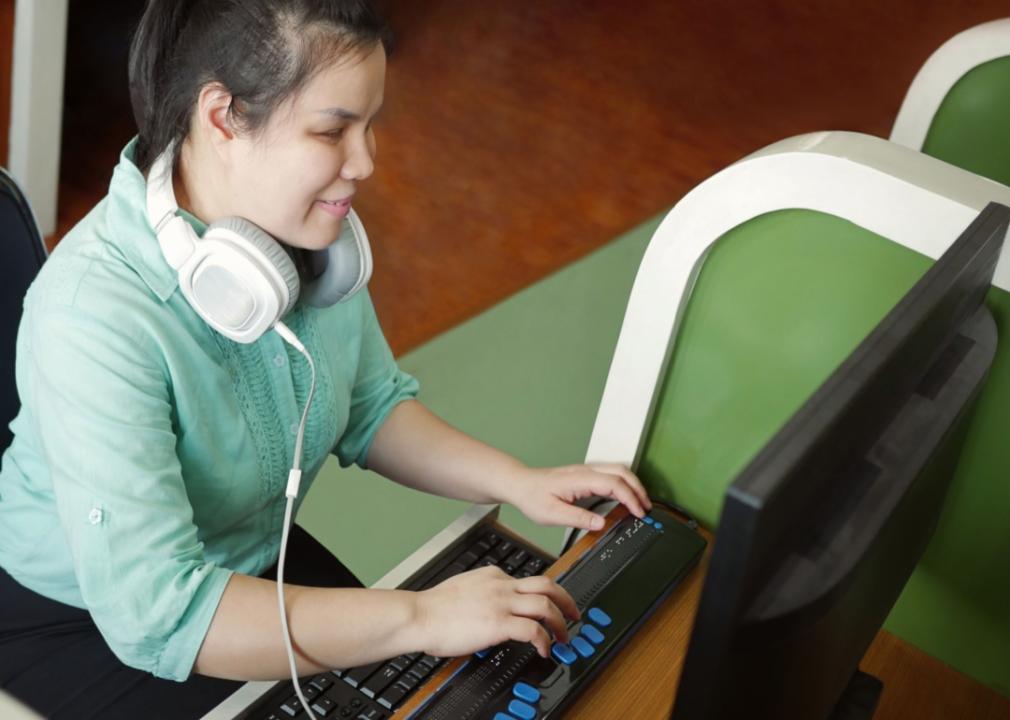 A woman with a visual disability sits at a computer using a specialized keyboard.