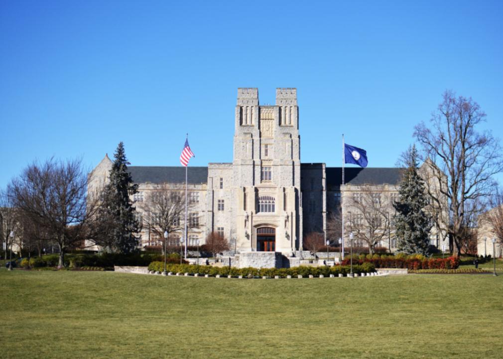 A large gray stone building with a tower in the middle and two flags flying in front of it.