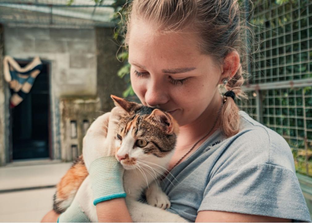 Woman holding a young kitten close to her chest.