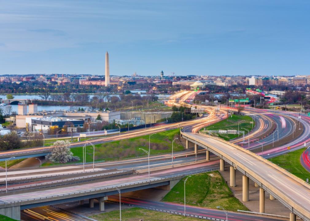 City skyline with a mix of shorter buildings and structures spreading out towards the edges of the image. A network of highways and roads can be seen crisscrossing the city.