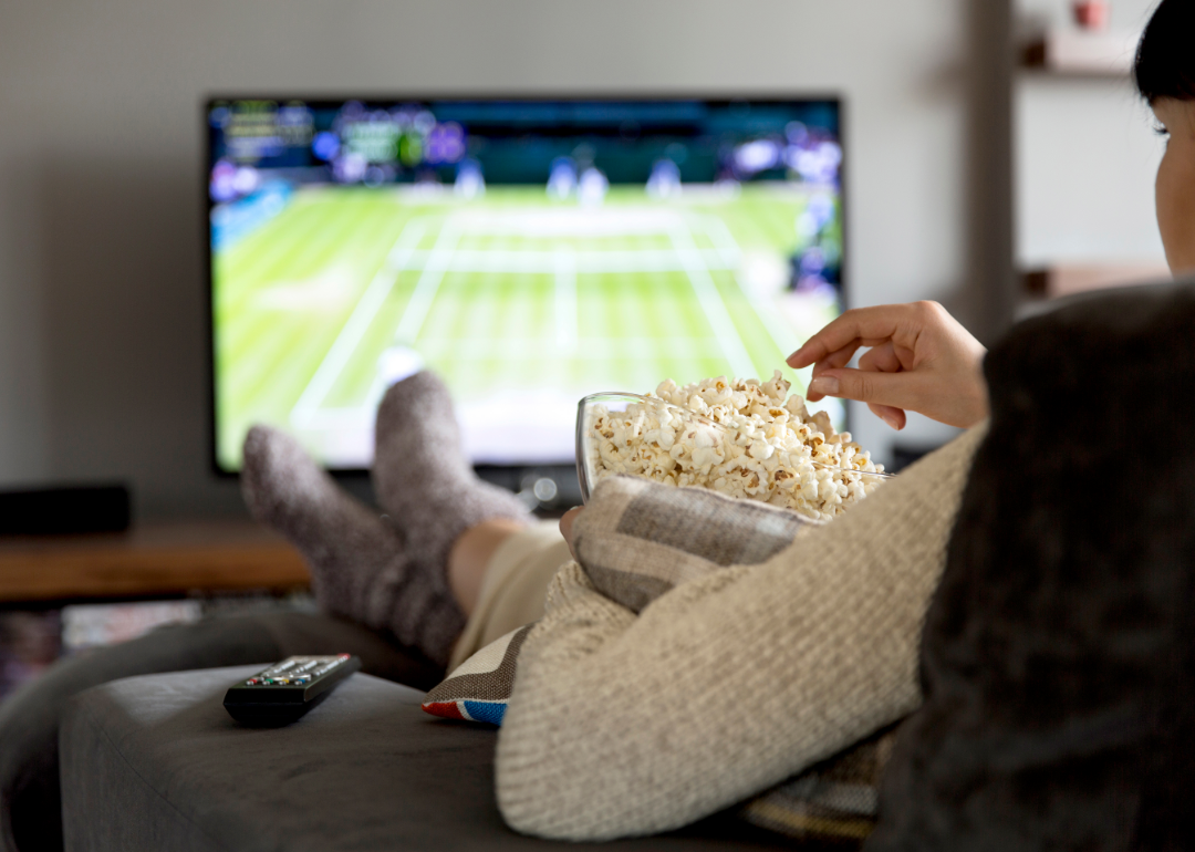 A young woman with popcorn watching sports on TV.