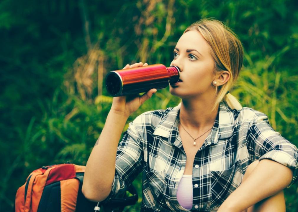 A hiker rests, drinks water from a reusable bottle.