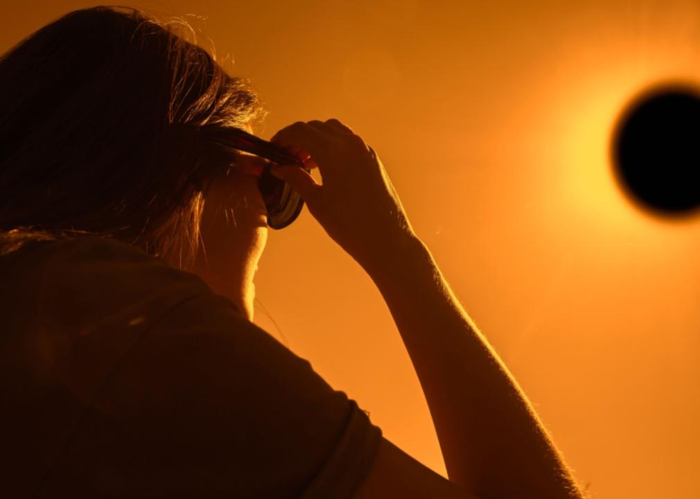 A close up of a woman looking at orange sky through sunglasses.