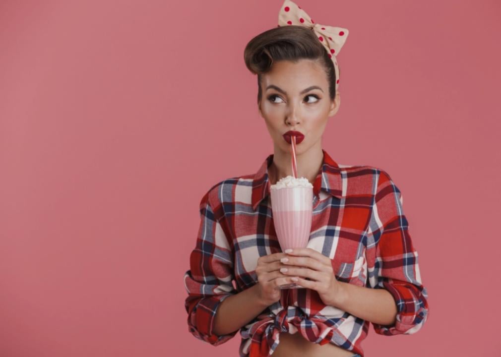 A brunette woman wearing a red checked shirt and holding a pink drink. 