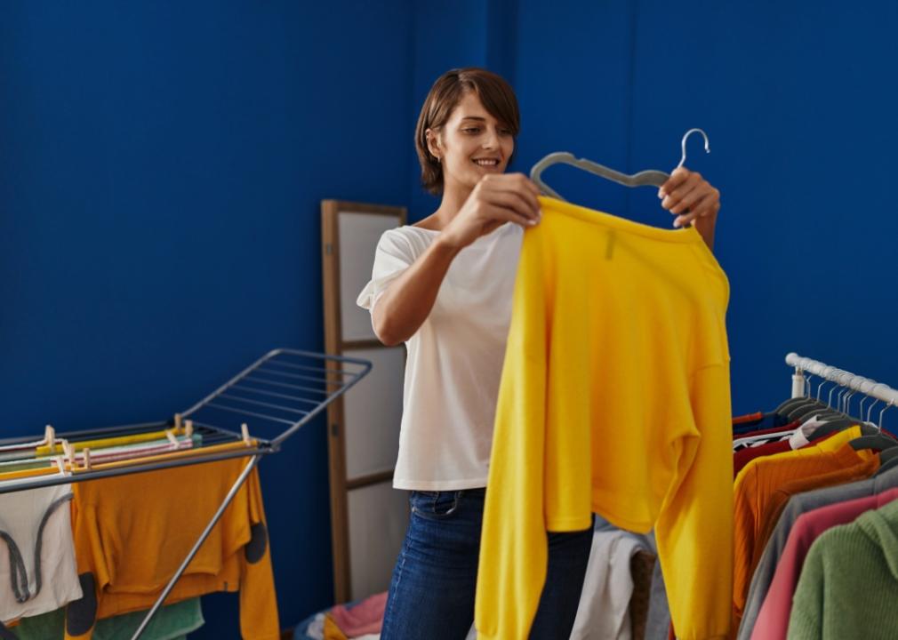 A woman holding up a yellow sweater on a hanger.