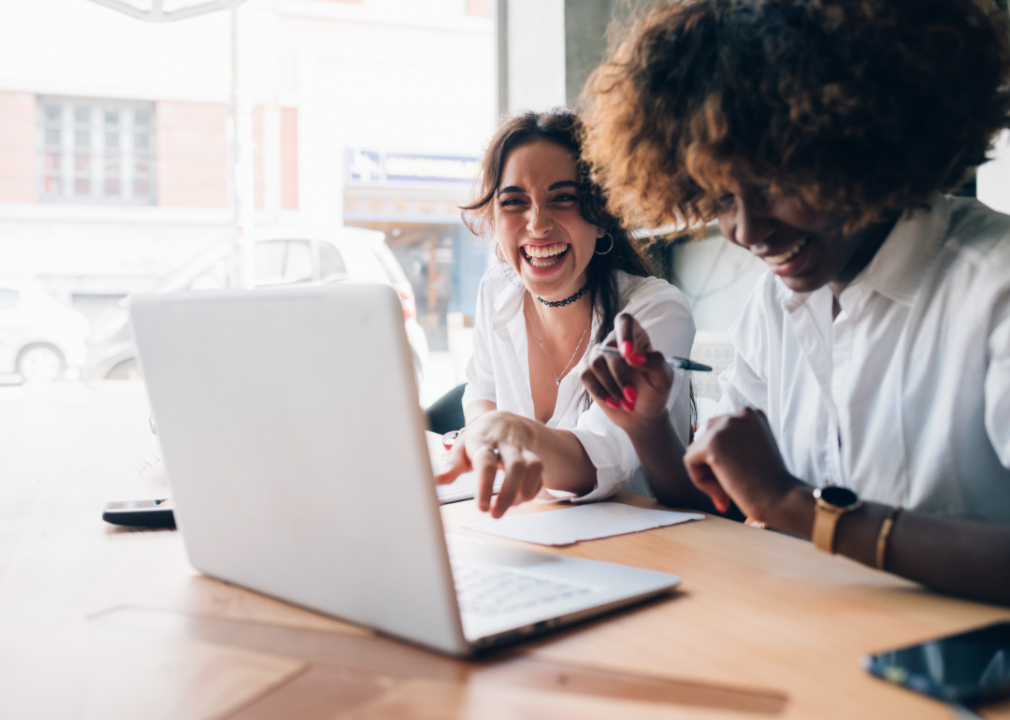 Two women laughing in front of a laptop.