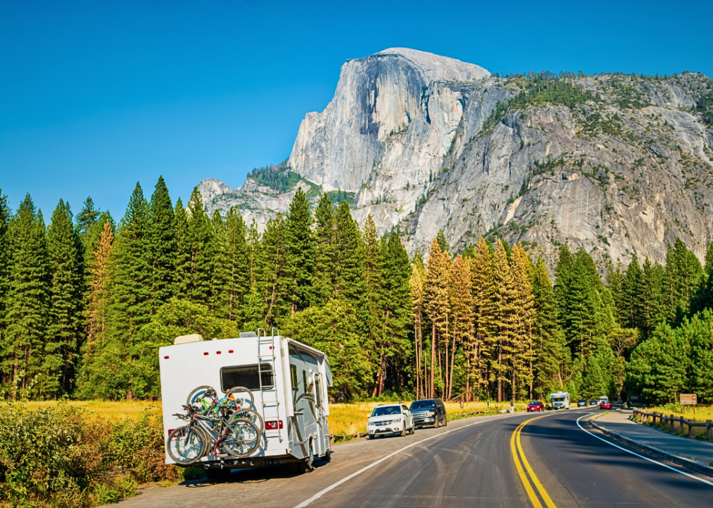 A motor home parked on the side of a quiet road with tall mountains in the background.