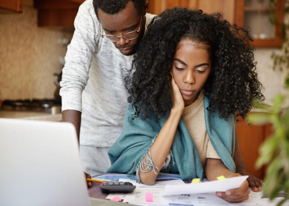 A young Black couple looking concerned while looking at their bills.