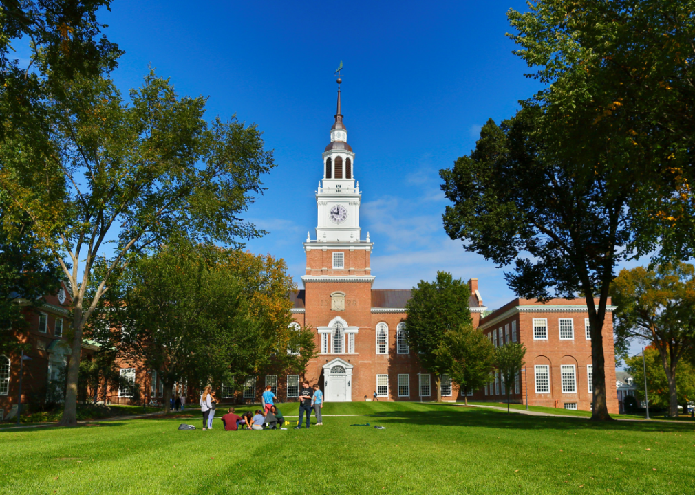 #8. Dartmouth College Students on a lawn in front of a red stone building with a clocktower.