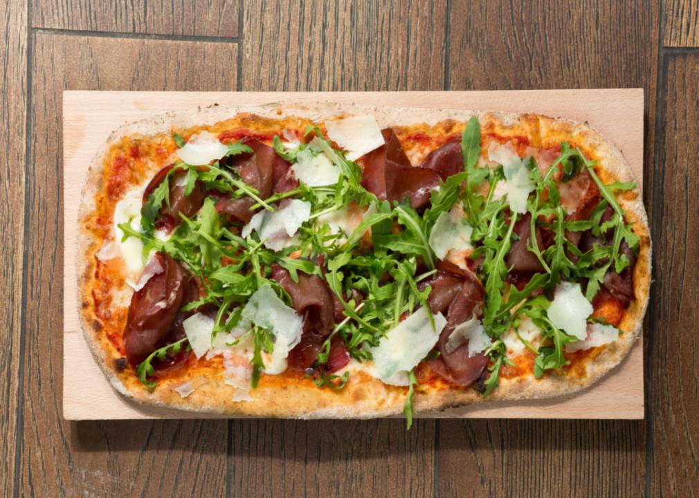 A long gourmet salami pizza with greens on a cutting board.