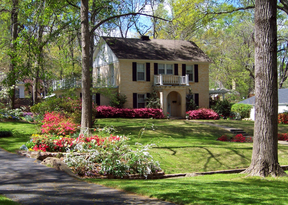 A country home with a large front yard surrounded by shaded trees and spring blooms