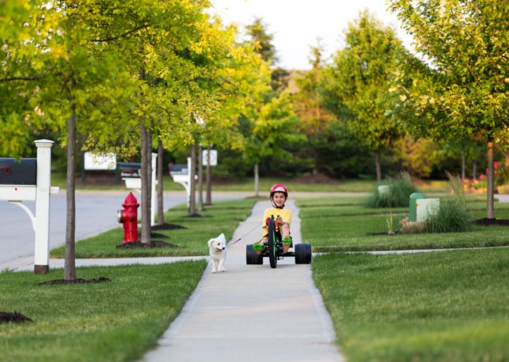 A boy on a tricycle on a neighborhood sidewalk.