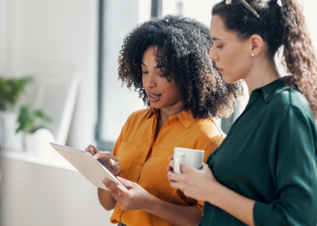 Two women look at a tablet in a bright office.