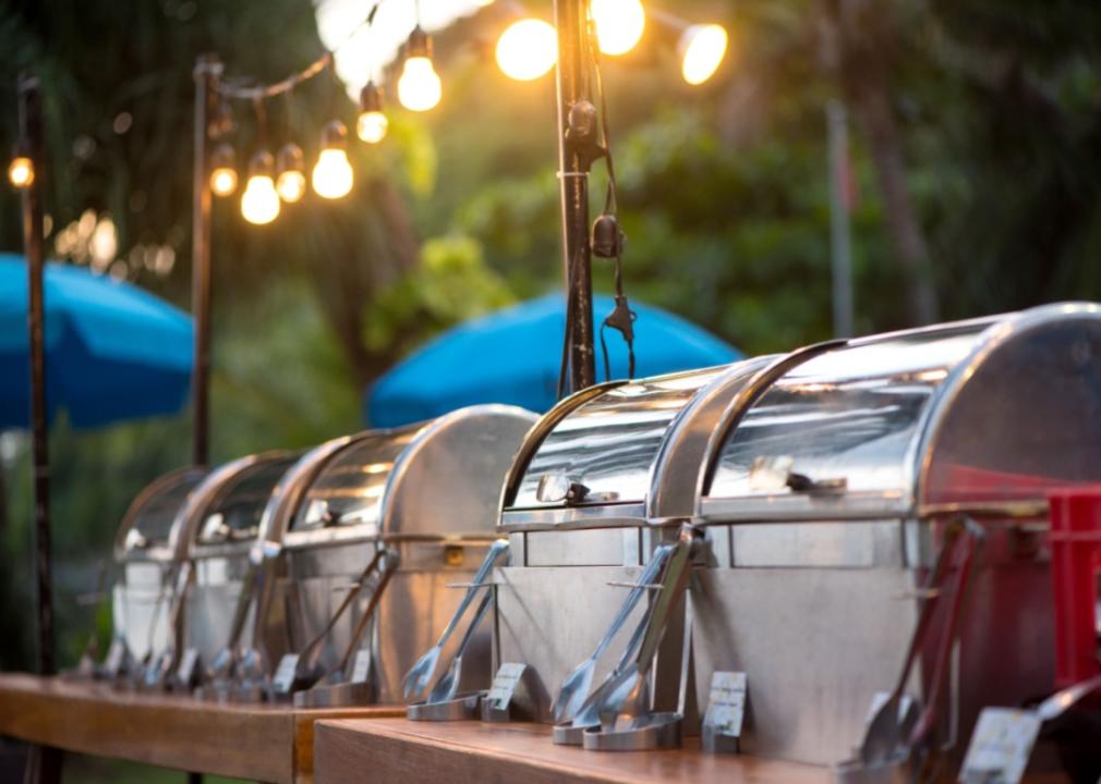 Large metal food warmers on a table outdoors.